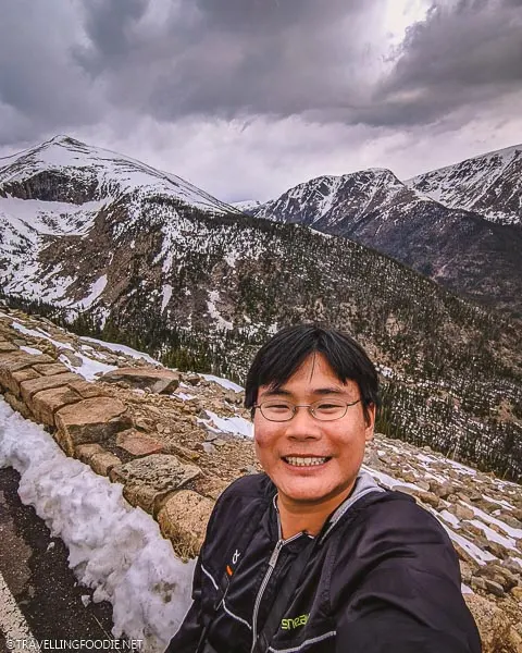 Raymond the Travelling Foodie with two snowy mountains at Rocky Mountain National Park