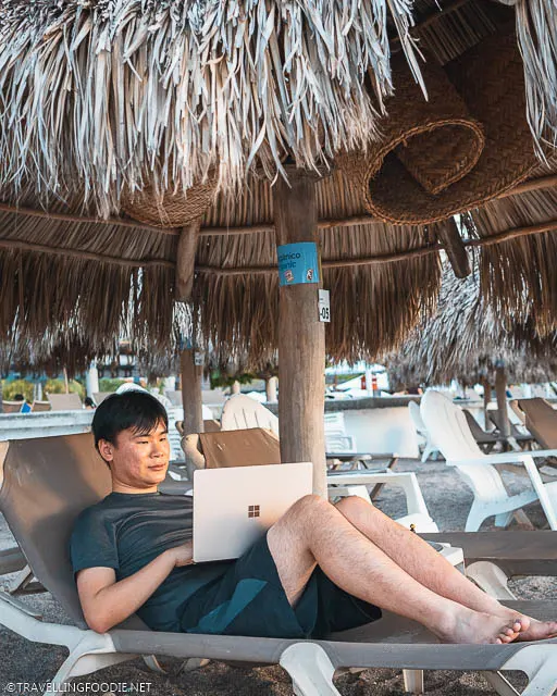 Travelling Foodie Raymond Cua lying on the cabana using Microsoft Surface Laptop 3