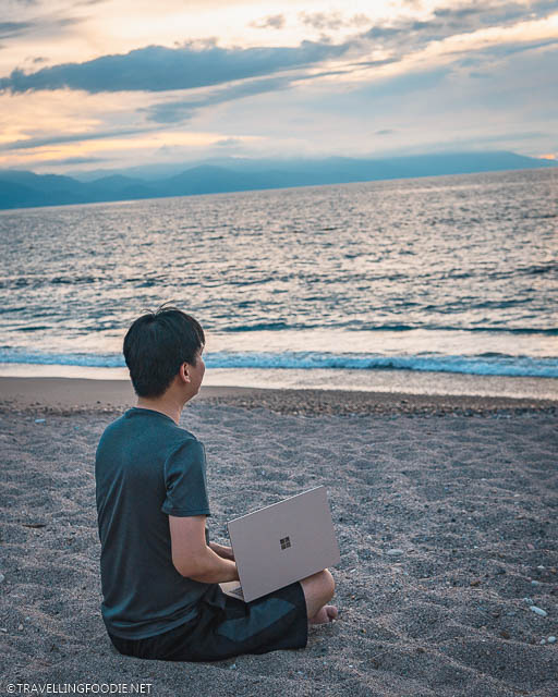 Travelling Foodie Raymond Cua with Microsoft Surface Laptop 3 on lap sitting on Playa Camarones in Puerto Vallarta