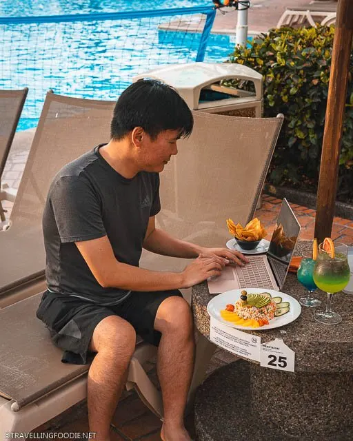 Travelling Foodie Raymond Cua sitting on pool chair using Microsoft Surface Laptop 3 on a table