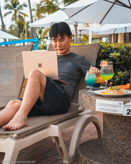 Travelling Foodie Raymond Cua grabbing nachos while using Microsoft Surface Laptop 3 on pool chair