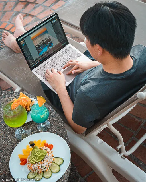 Over the shoulder of Travelling Foodie Raymond Cua editing photo on Microsoft Surface Laptop 3 with cocktails and food