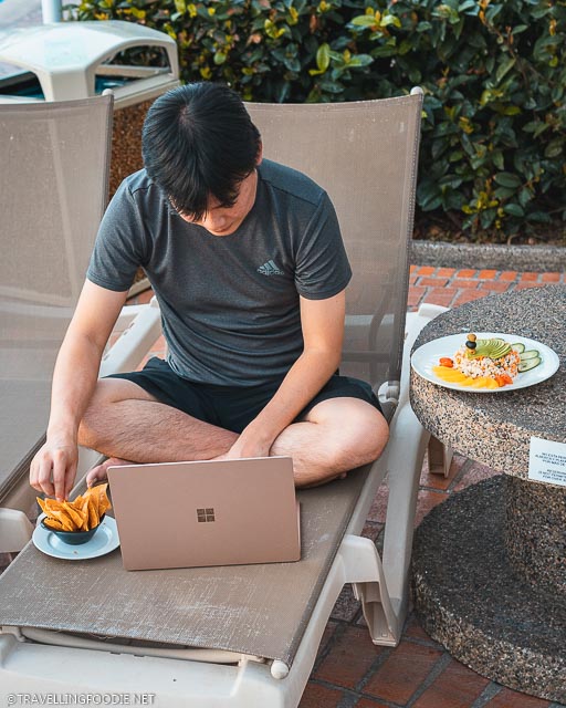 Travelling Foodie Raymond Cua grabbing nachos while working on Microsoft Surface Laptop 3 on pool chair