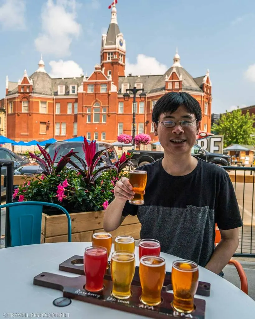 Travelling Foodie Raymond Cua with Beer Flight at Heritage Hops Brewery with Stratford City Hall behind