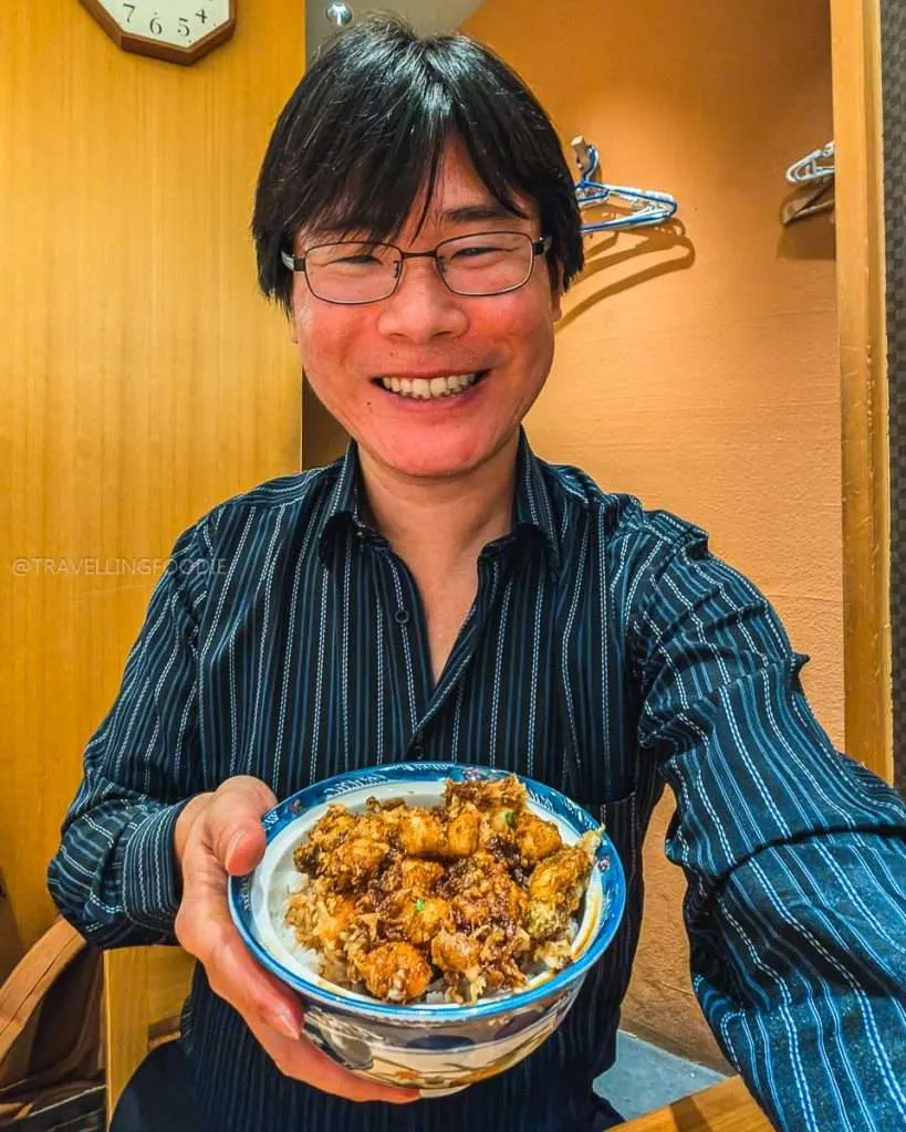 Man holding a bowl of tempura kakiage rice in Tokyo, a meal discovered with Japan travel apps.