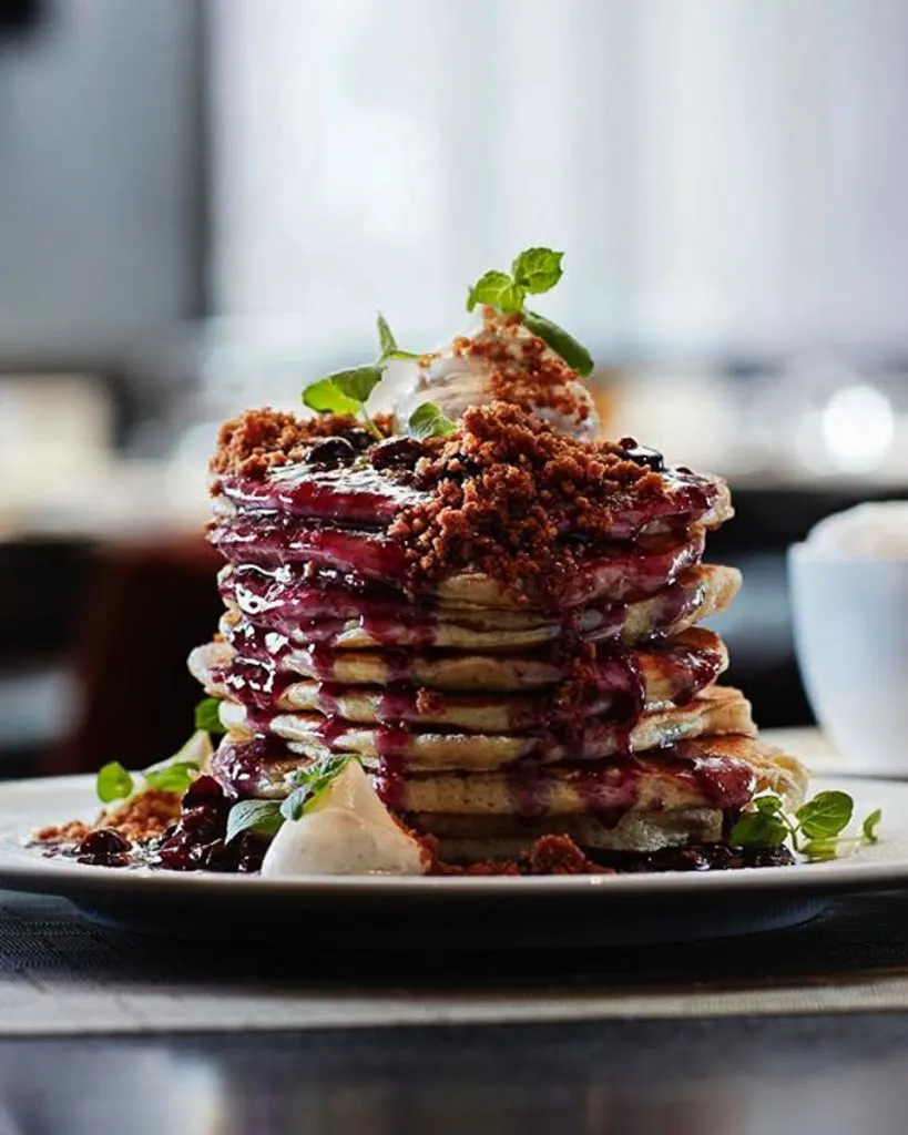 Stack of fluffy Blueberry Buttermilk Pancakes from ONE Restaurant topped with blueberry compote and vanilla cream cheese.