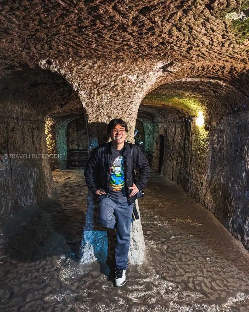 Raymond Cua standing by a stone pillar in a large room within the ancient Derinkuyu Underground City in Turkey