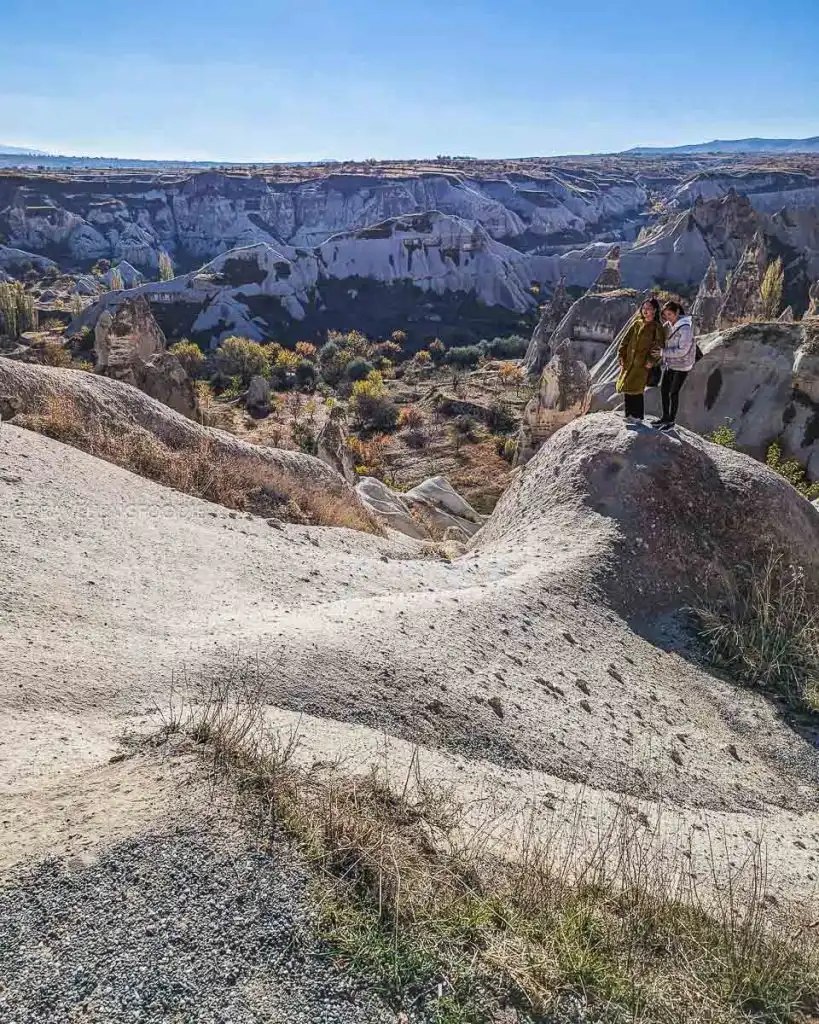 Tourists standing on a rock formation at Goreme Panorama overlooking the Pigeon Valley and Uchisar Castle distance