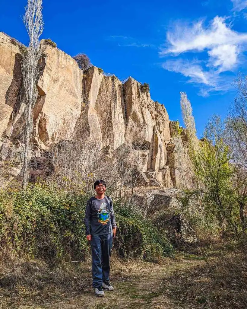 Travelling Foodie Raymond Cua hiking in Ihlara Valley with massive canyon walls and rock-cut caves in the background