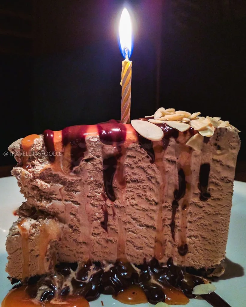 Close up of a free birthday Billy Miner Pie slice from Canada's The Keg featuring mocha ice cream, chocolate crust, hot fudge, caramel, almonds, and a lit birthday candle.