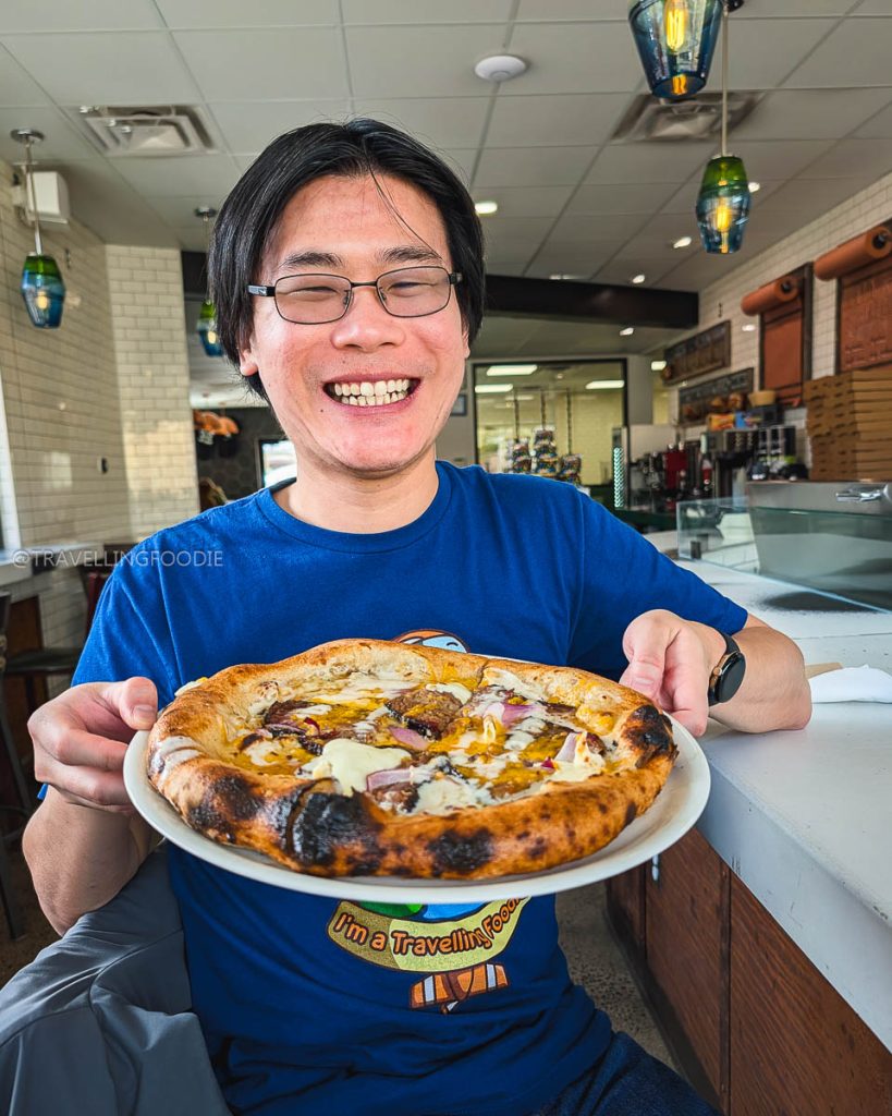 Travelling Foodie Raymond Cua holding the Cowboy Beef Brisket Pizza at Alibi Pizzeria, exploring where to eat in Laramie.