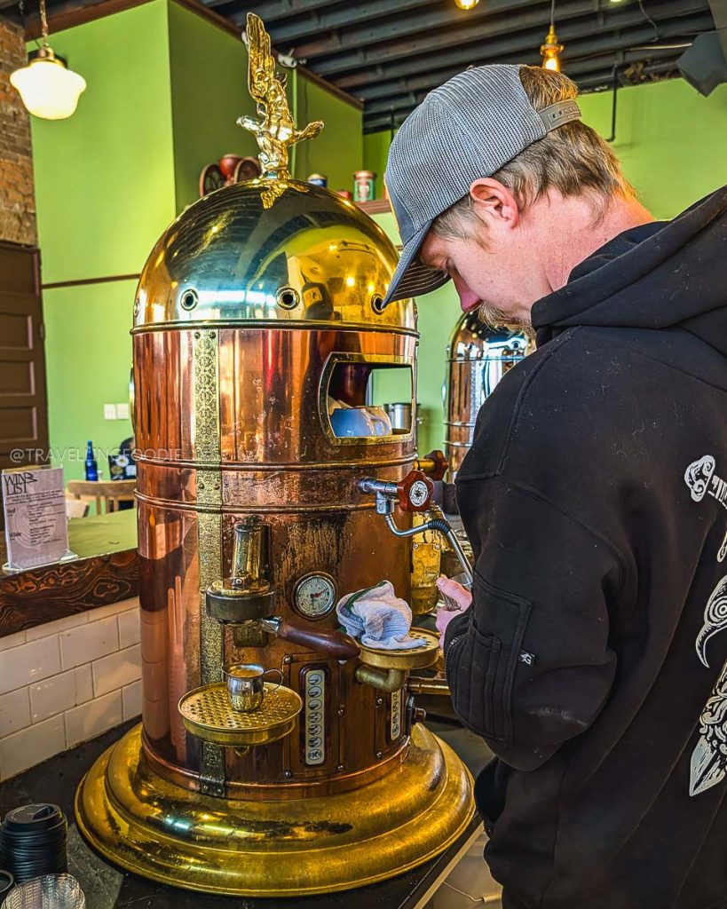 Barista making specialty coffee with a gold espresso machine, a unique thing to do in Laramie cafes.