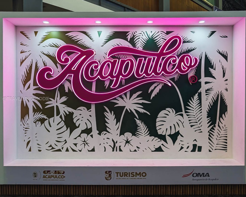 Bright pink neon Acapulco sign with tropical palm leaf designs displayed at Aeropuerto Internacional General Juan N. Álvarez