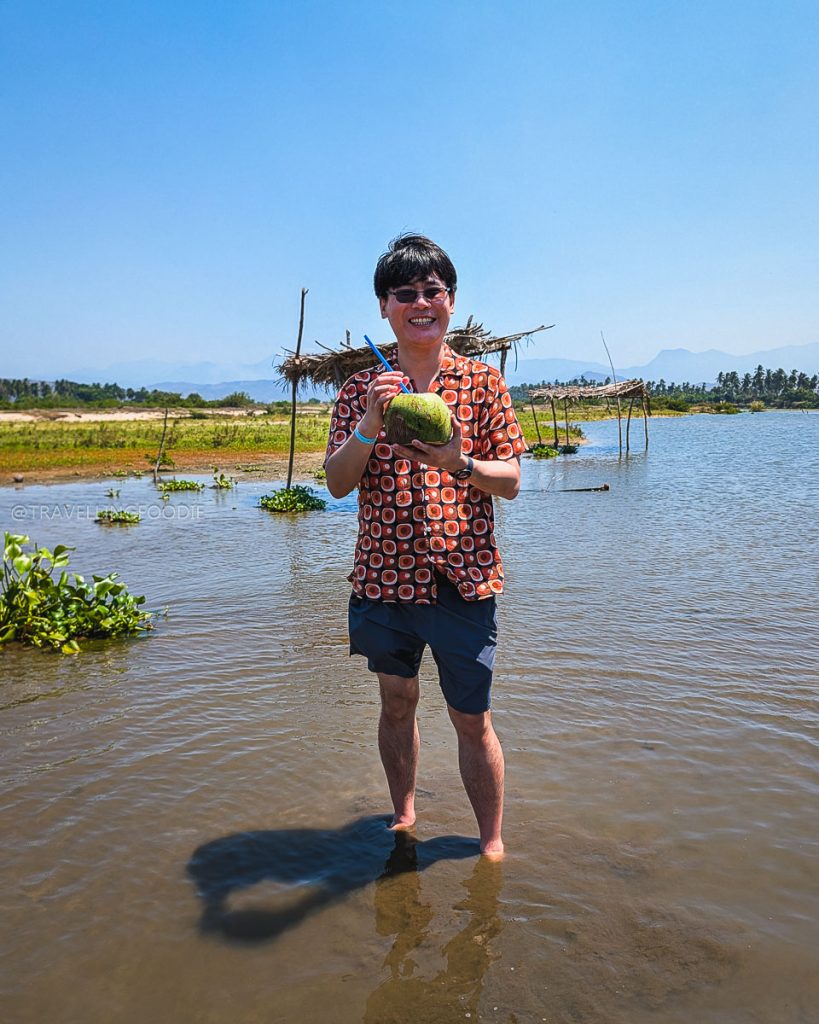 Travelling Foodie Raymond Cua standing in Coyuca Lagoon water drinking a fresh coconut in Acapulco.