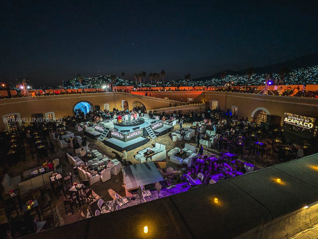 Nighttime view of the Tianguis Turistico event at Fort San Diego with illuminated Acapulco city lights.