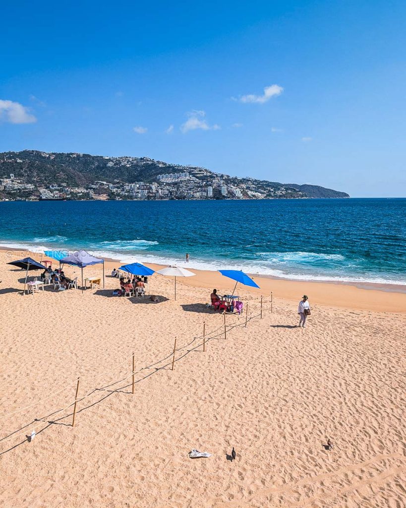 Relaxing on the golden sands of Playa Icacos under blue umbrellas, one of the best beaches in Acapulco Golden Zone.