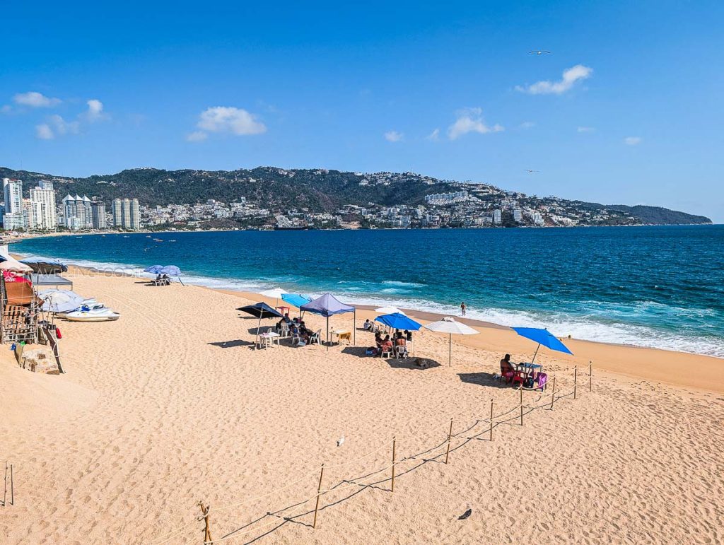 Scenic daytime view of Playa Icacos coastline in Acapulco, featuring blue ocean waters and distant mountain landscapes.