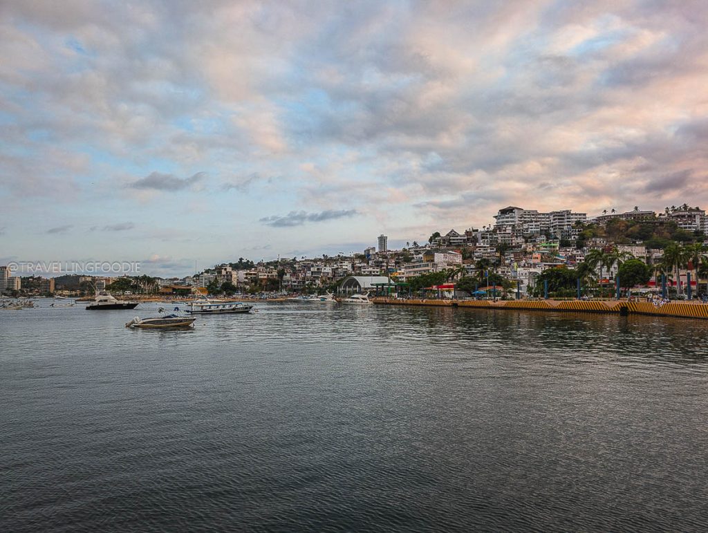 Beautiful sunset view over Acapulco Bay featuring docked boats and the vibrant city skyline built into the coastal hills.