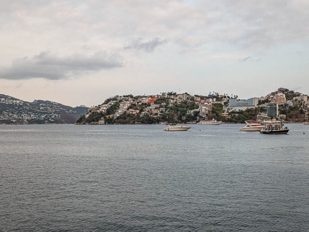 Wide view of boats sailing in the calm waters of Acapulco Bay surrounded by stunning coastal mountains and city buildings.