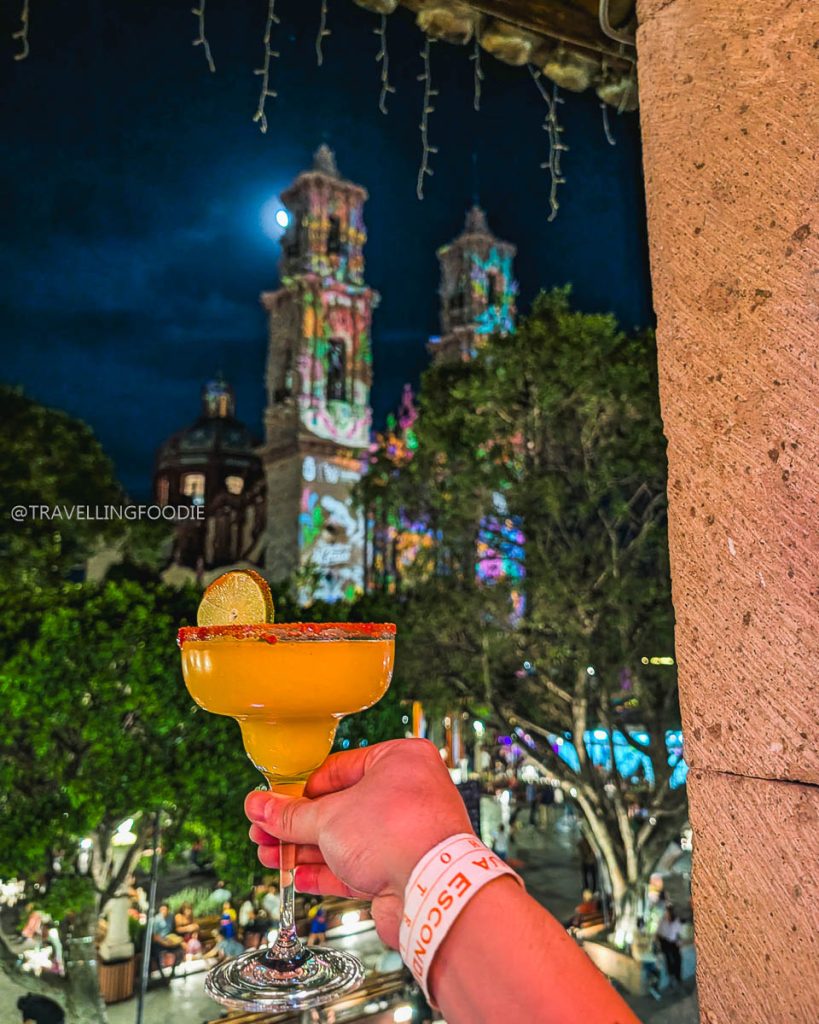 Holding a refreshing mango margarita at La Bendita at night, with the illuminated Santa Prisca church in Taxco.