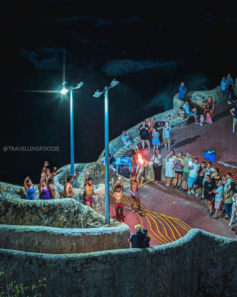 Professional La Quebrada cliff divers holding fire torches at night, preparing for an iconic dive in Acapulco.