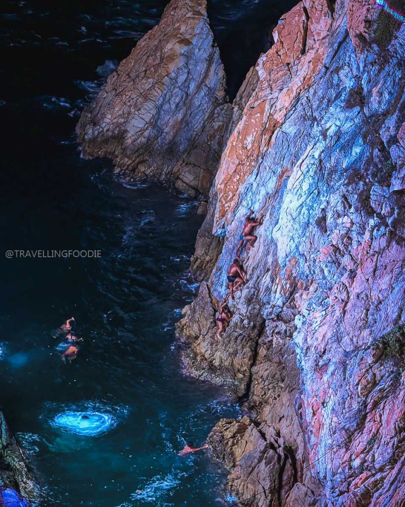 Brave La Quebrada cliff divers scaling the steep illuminated rock face at night, a famous Acapulco attraction.