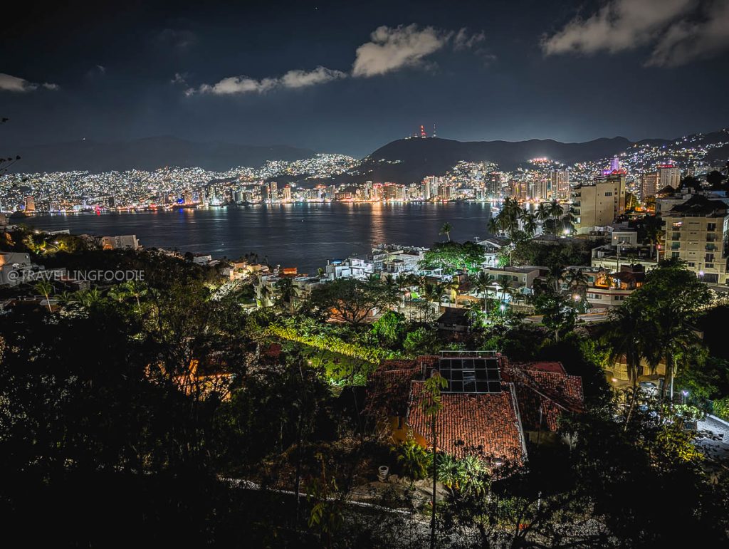 Stunning panoramic night view of Acapulco Bay, showcasing vibrant city lights from an elevated scenic viewpoint.