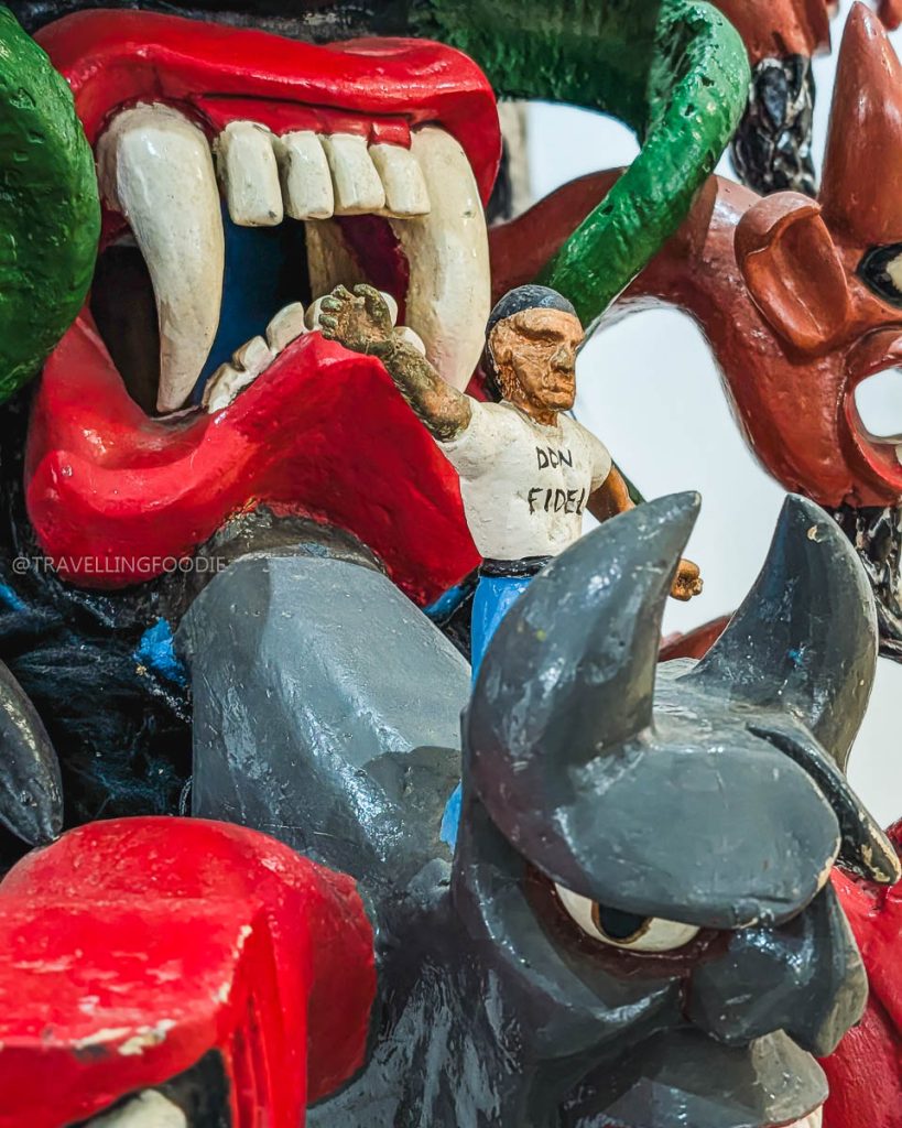 Close-up of a vibrant horned mask with a small Don Fidel figure, a fascinating detail at the Acapulco Mask Museum.