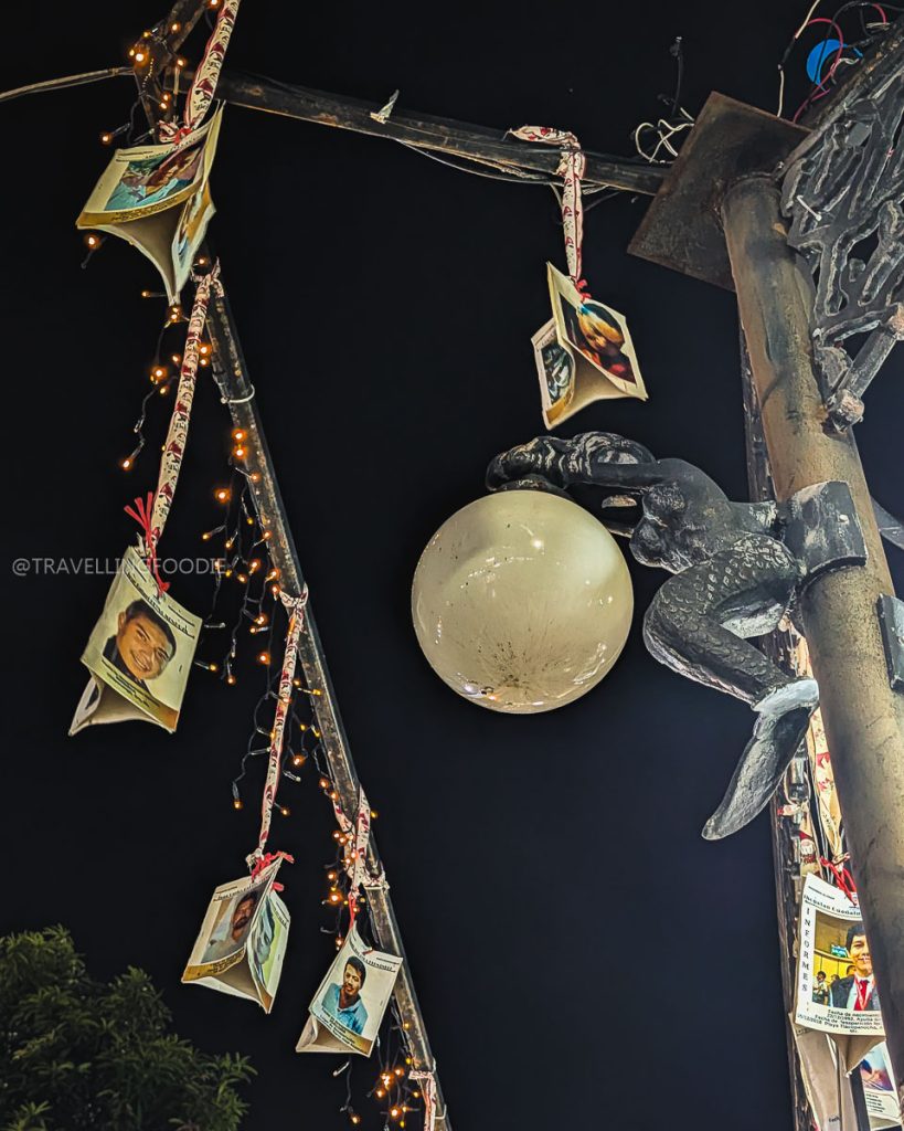 Nighttime view of a decorative street lamp featuring a mermaid sculpture and hanging photos in Acapulco's Plaza Alvarez.