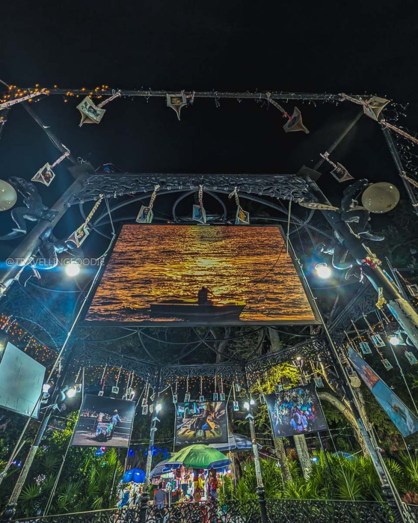 Illuminated gazebo and glowing photography surrounded by hanging photos at night in the historic Plaza Alvarez, Acapulco.