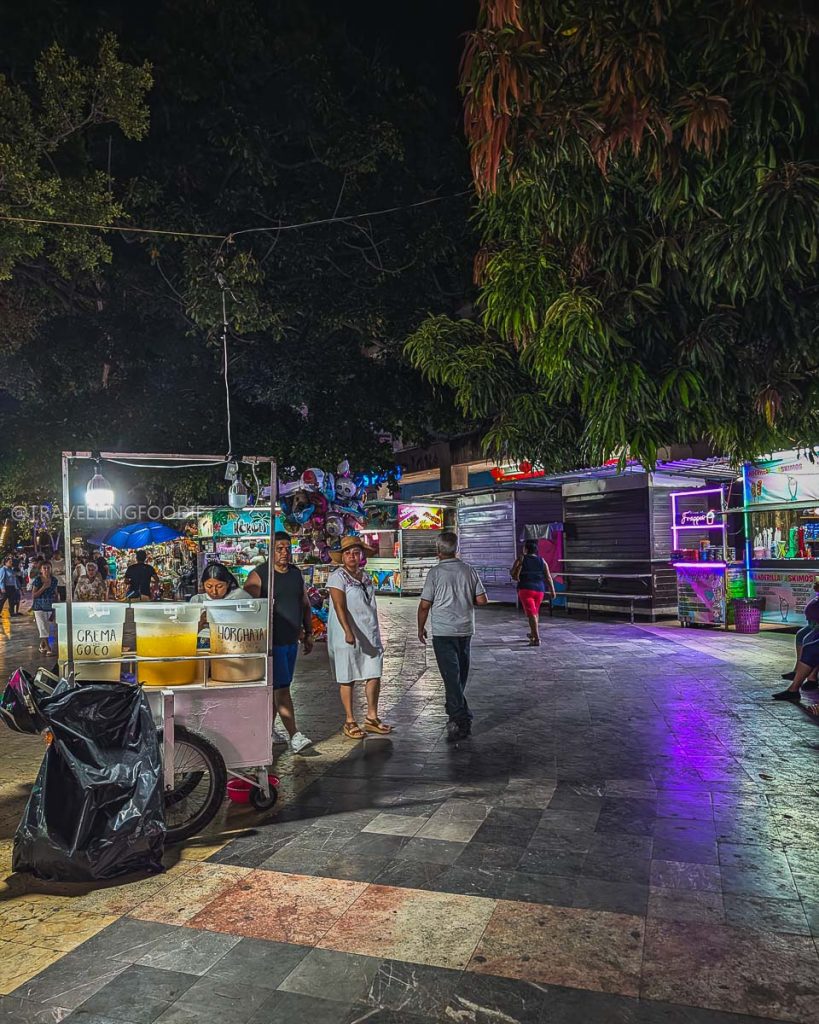 Vibrant night street food cart selling fresh crema and horchata under the trees at Plaza Alvarez in Acapulco.