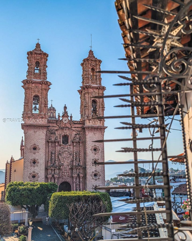 Beautiful morning view of the iconic Santa Prisca church towers framed by rustic ironwork in Taxco de Alarcon.