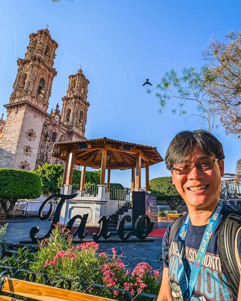 Raymond Cua, the Travelling Foodie, at the Taxco sign and gazebo with the beautiful Santa Prisca church in the background.