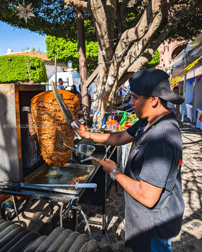 Mexico City vendor expertly carving al pastor meat from a massive trompo at the El Gran Taco festival in Taxco.