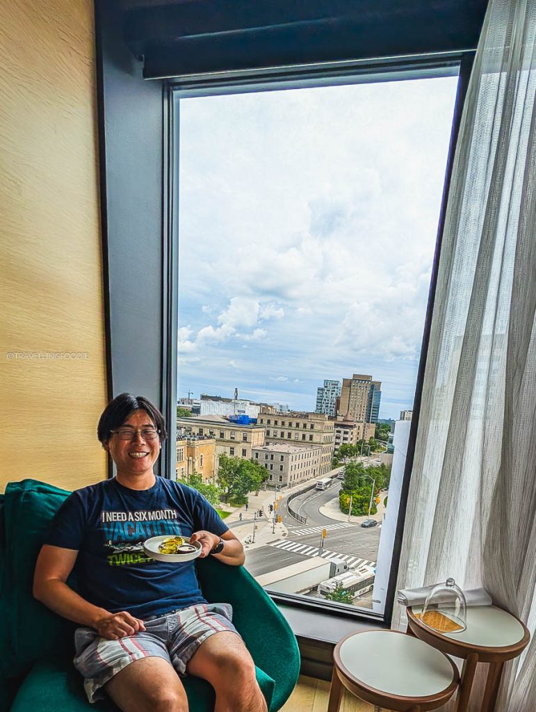 Travelling Foodie holding a welcome plate with a scenic window view at Le Germain Ottawa.