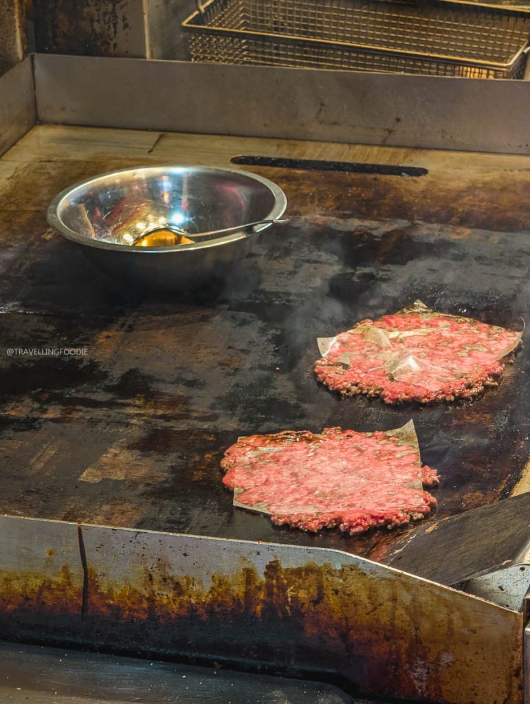 Smash burger patties sizzling on the grill at Deadly Dan's Burgers, a top spot for Saskatoon food.