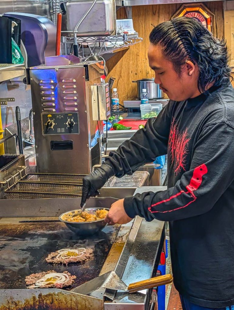 Cook preparing fresh smash burgers on the grill at Deadly Dan's Burgers, a great local place to eat in Saskatoon.