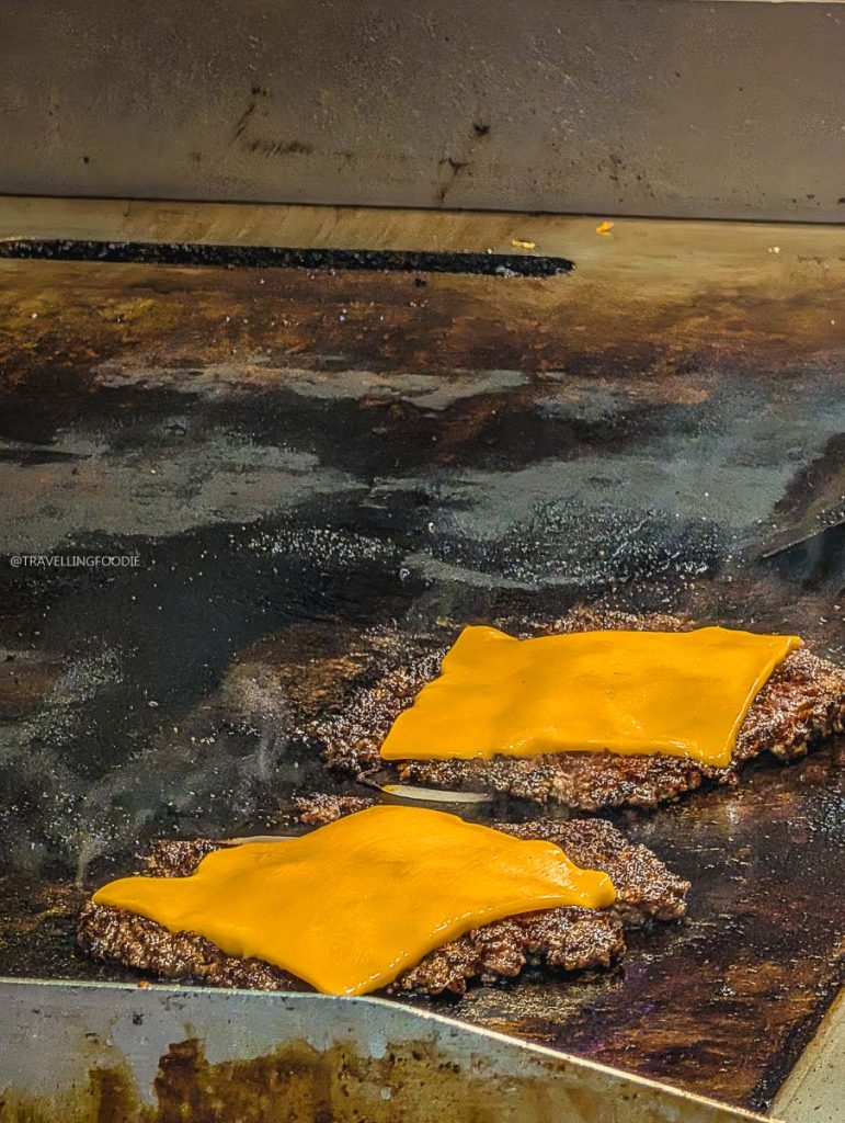 Smashed burger patties with melting cheese on the grill at Deadly Dan's Burgers, among top Saskatoon local restaurants.