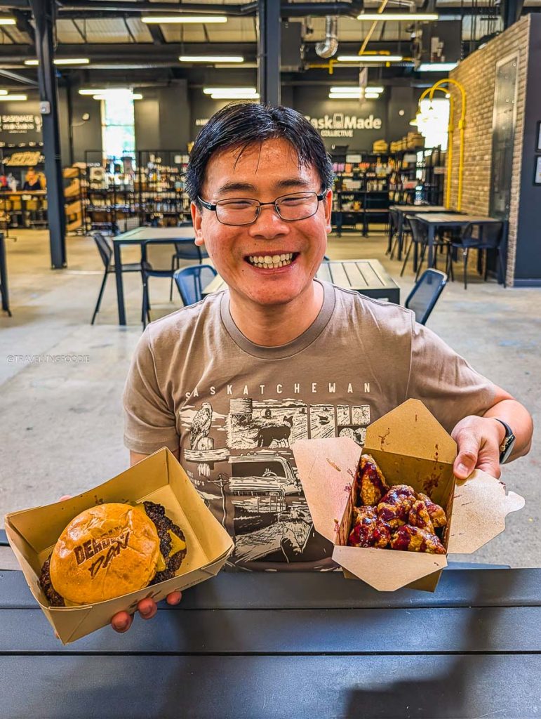 Travelling Foodie Raymond Cua holding a burger and wings from Deadly Dan's Burgers, showing exactly where locals eat in Saskatoon.