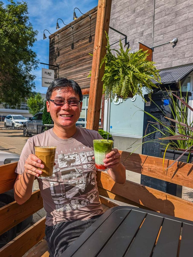 Travelling Foodie Raymond Cua holding an iced latte and matcha on the patio at Out of Order Coffee, one of the best Saskatoon coffee shops.