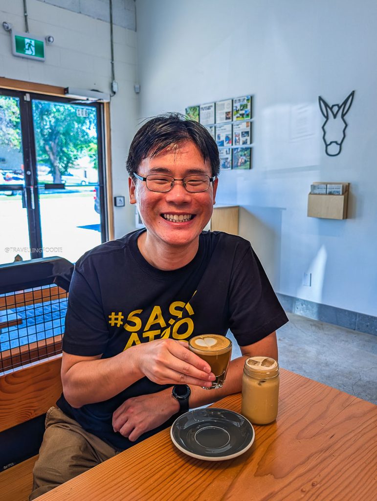Travelling Foodie Raymond Cua holding a fresh cortado at The Colombian, showing foodies exactly where locals eat in Saskatoon.