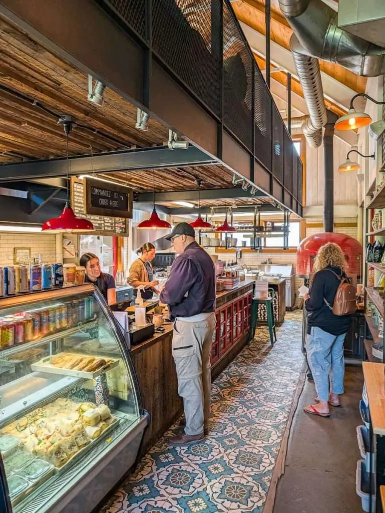 Customers ordering at the counter and pastry case inside Biscotti & Cie with a red pizza oven in the background.