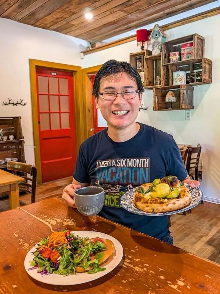 Travelling Foodie Raymond Cua holding a coffee and an Eggs Benedict pizza for breakfast at Biscotti & Cie during an Outaouais road trip.