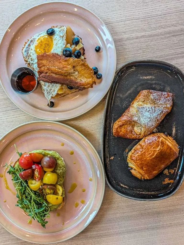 Plates of Chez Edgar French Toast with pork belly, avocado toast, and fresh pastries from Cafe Palmier in Chelsea.