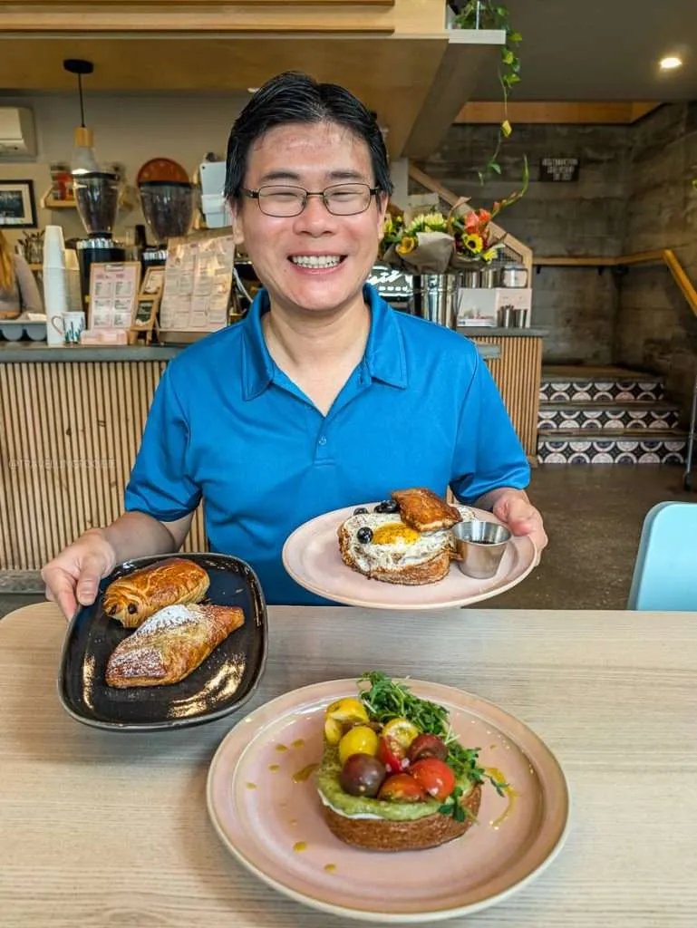 Raymond Cua holding plates of sweet and savory French toast and pastries for brunch at Cafe Palmier in Chelsea.