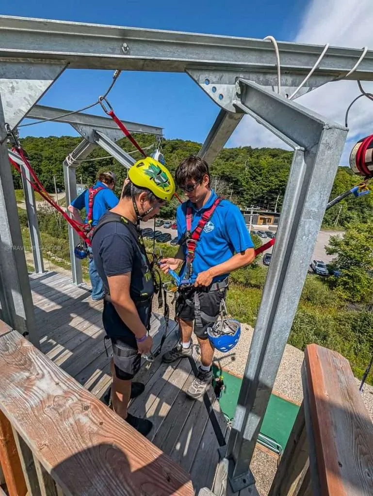 A guide securing Raymond Cua's harness on the Peak to Peak drop zone platform at Camp Fortune in Chelsea.