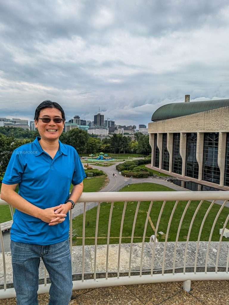 Raymond Cua smiling on the museum viewing deck overlooking Parliament Hill, a top Gatineau attraction.