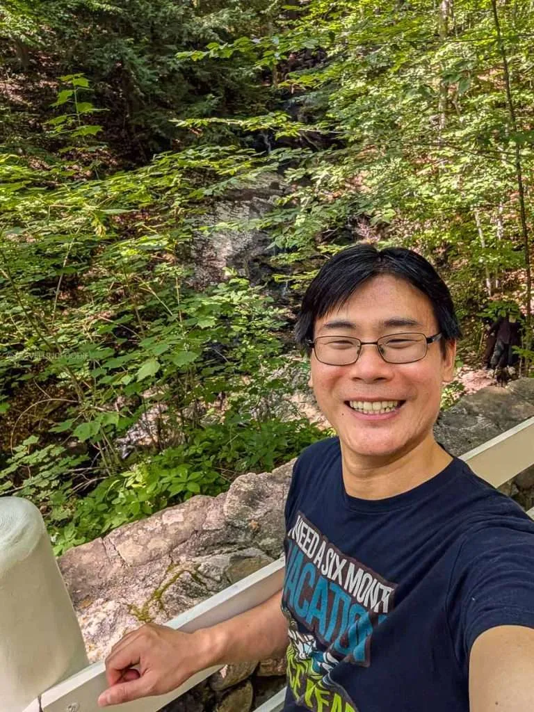 Raymond Cua smiling in front of the serene Bridal Veil Falls at the Mackenzie King Estate in Gatineau Park, Chelsea.