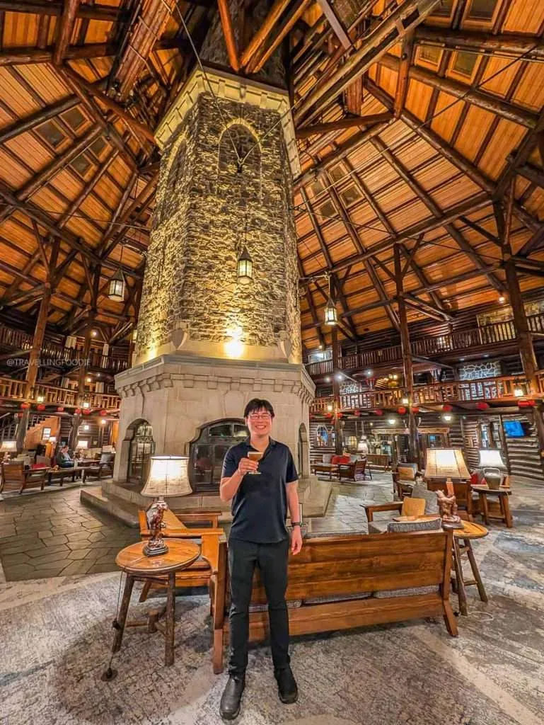 Raymond Cua holding a drink by the massive six-sided stone fireplace inside Fairmont Le Chateau Montebello.