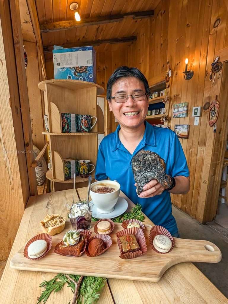 Travelling Foodie Raymond Raymond Cua holding chaga mushroom with a tray of Indigenous pastries at Kisisam Patisserie.
